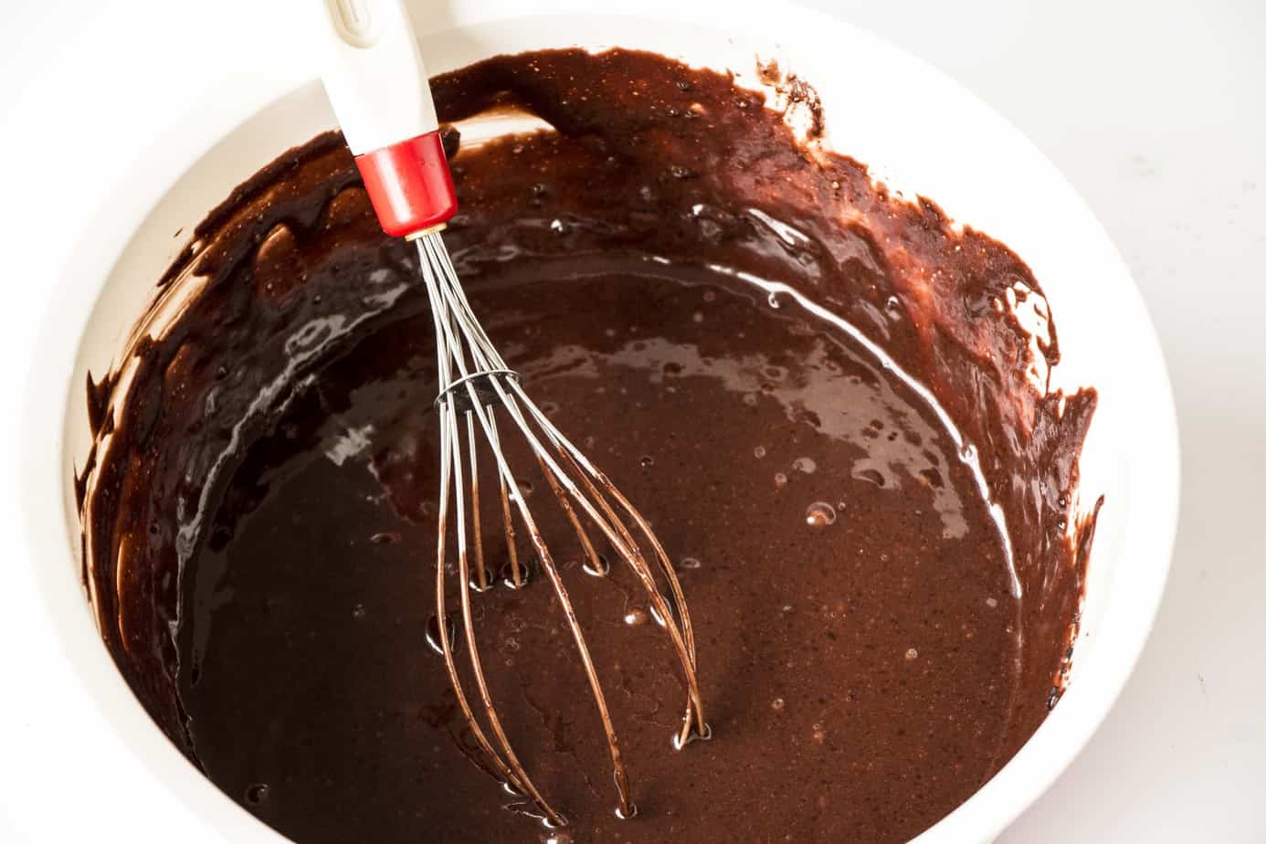 A bowl of chocolate batter in a white bowl with a whisk.