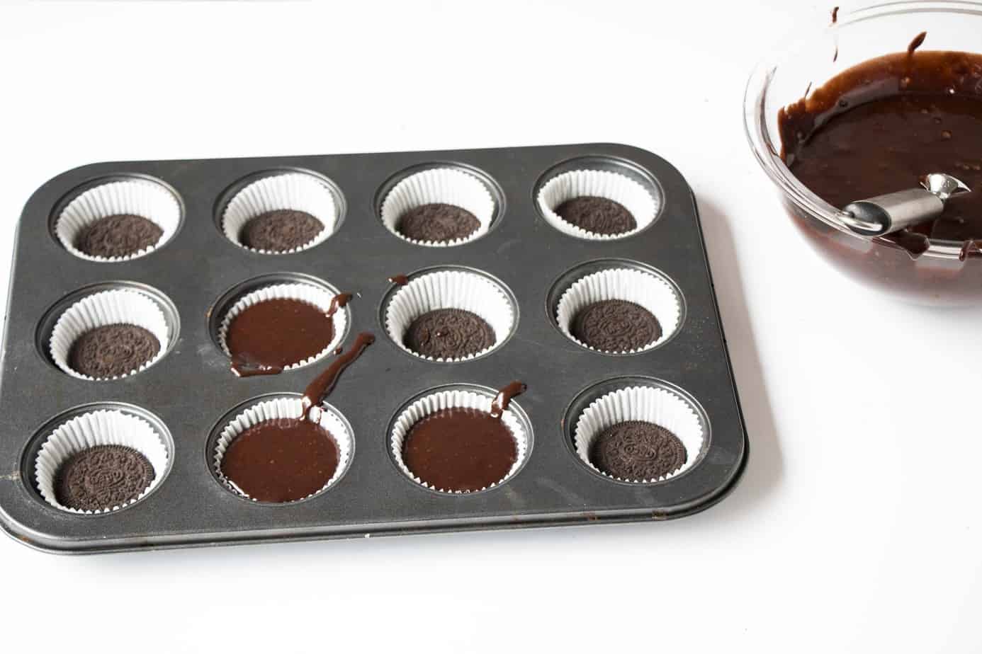 A pan filled with cupcake liners and a Oreo cookie at the bottom of each one.