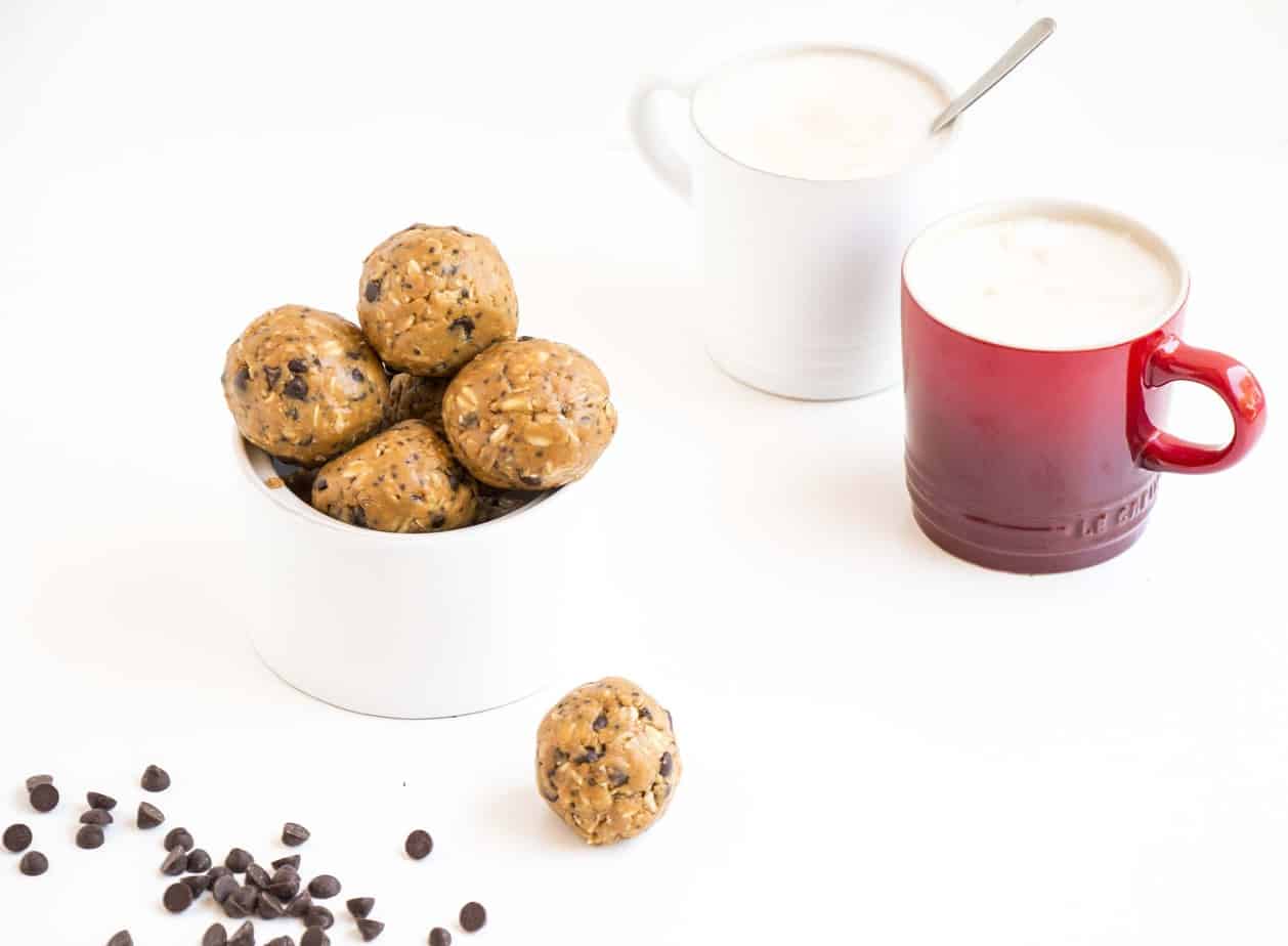 A bowl of protein balls with two mugs of coffee.