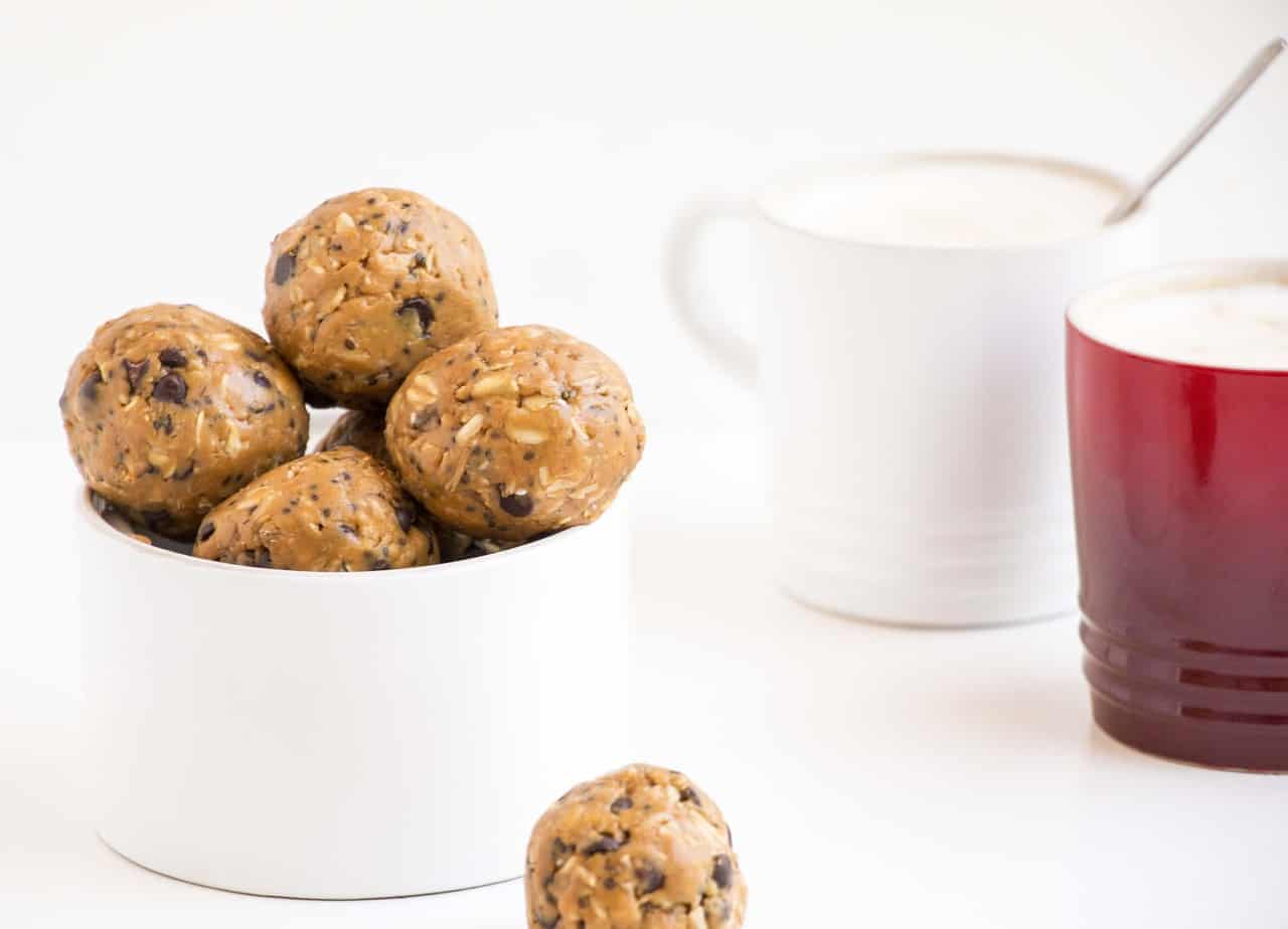A bowl of protein balls with two mugs of coffee.