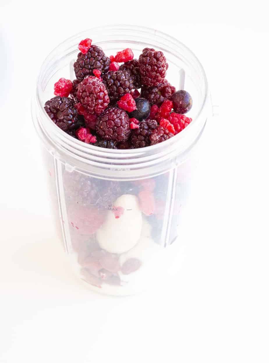 A blender filled with berry smoothie ingredients.