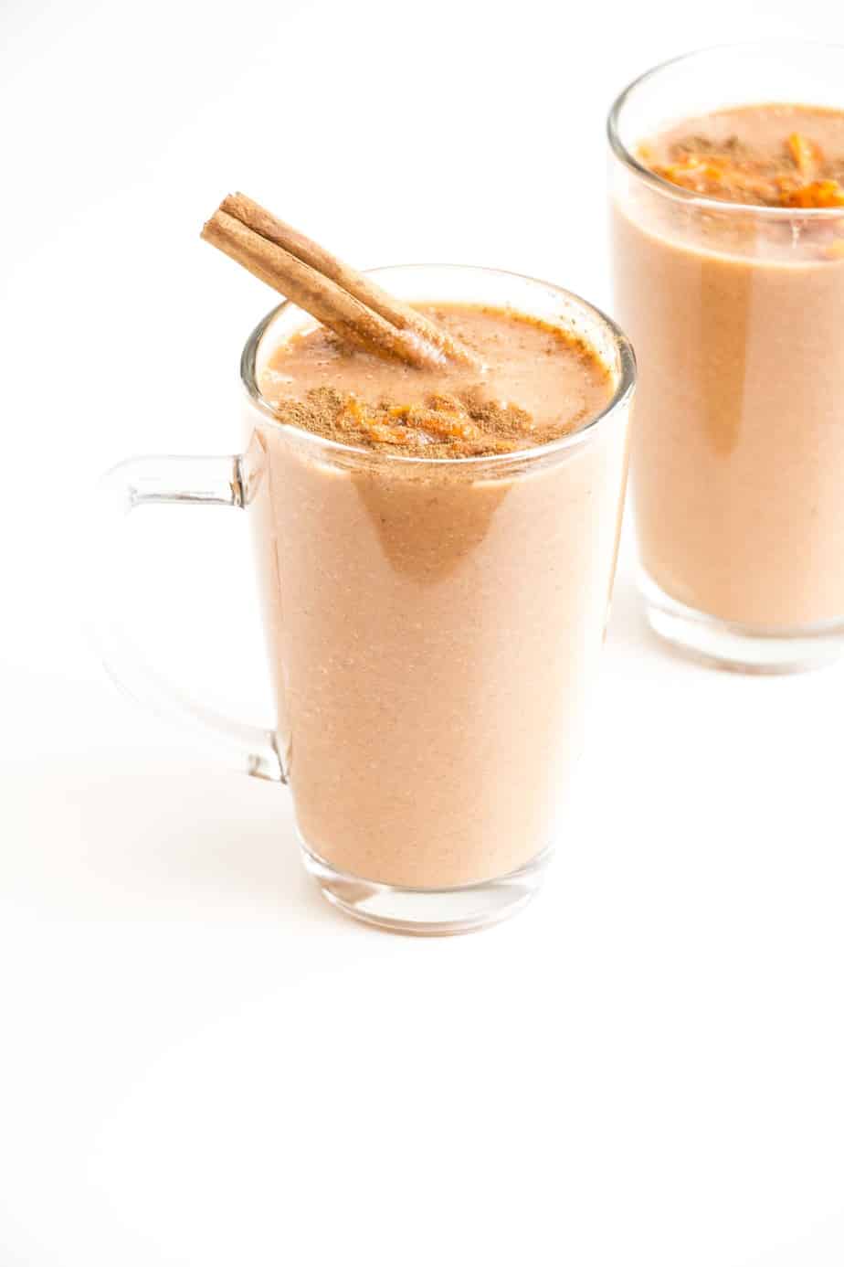 A carrot smoothie in a serving glass with a cinnamon quill.