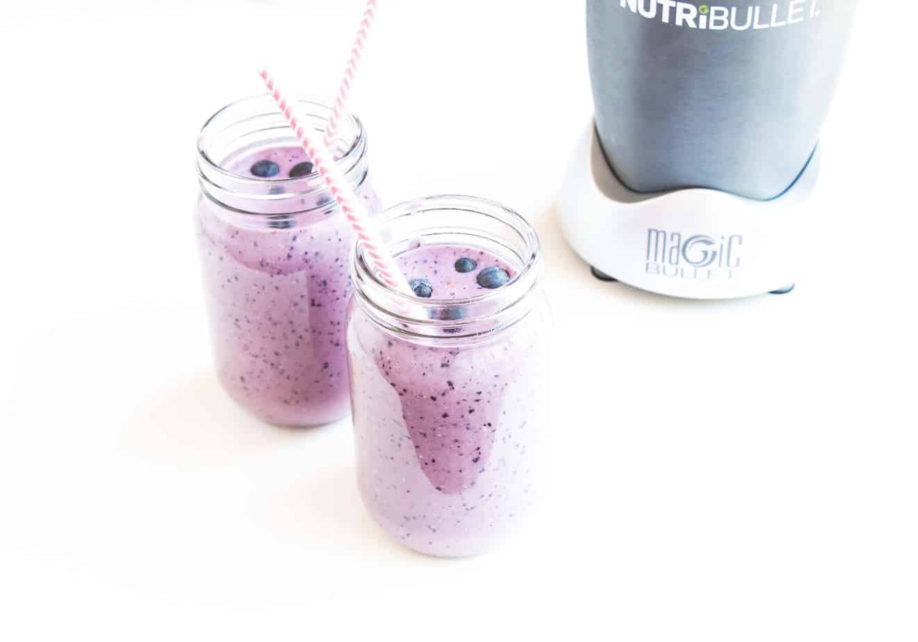 Two blueberry smoothies with fresh blueberries and straws.