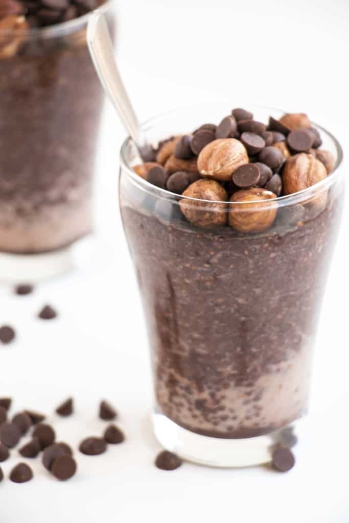 A glass of chocolate pudding with a spoon and chocolate chips.