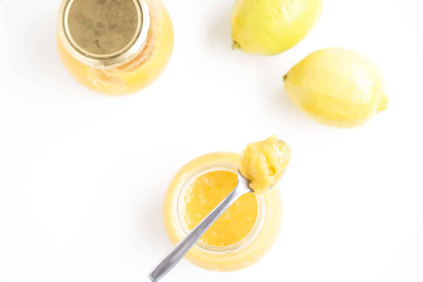 Jars of lemon curd with a spoonful of curd on a teaspoon resting on top of the one jar.
