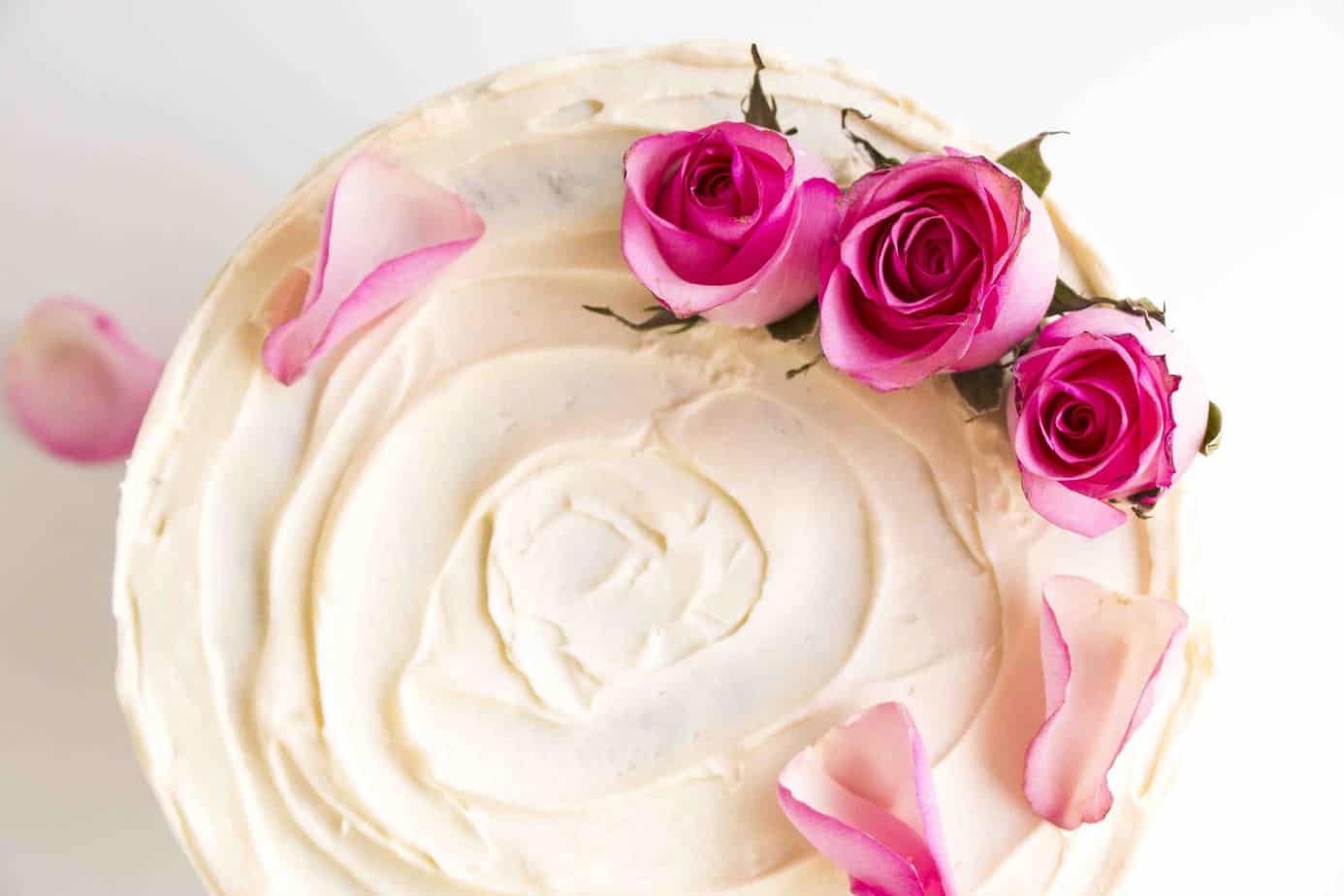 Pink roses on top of a frosted cake.