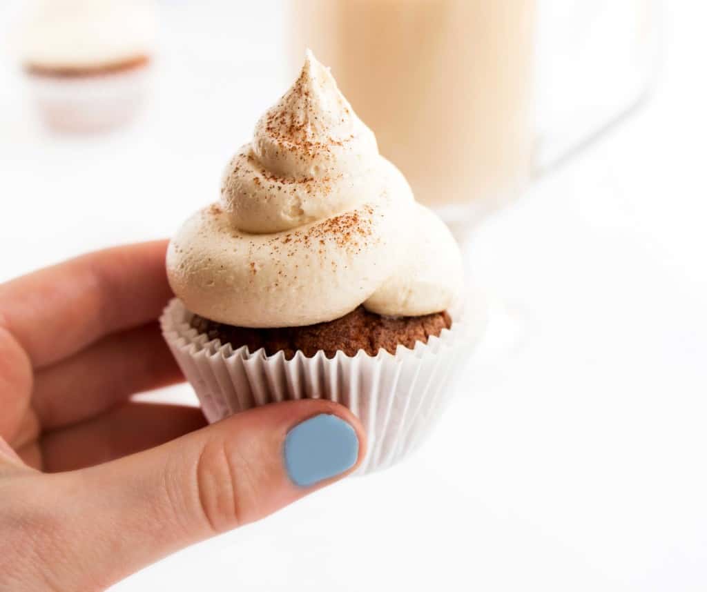 A hand holding a cupcake with frosting.