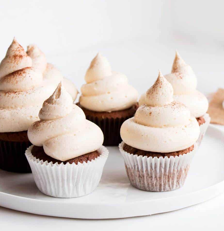 A plate of frosted chai cupcakes dusted with ground cinnamon.