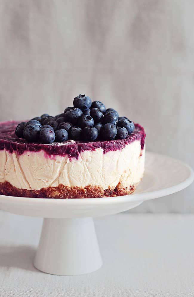 A blueberry cheesecake on white cake stand.