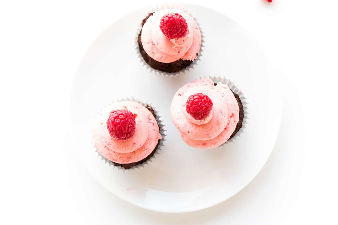 Three cupcakes that are frosted and on a white plate.