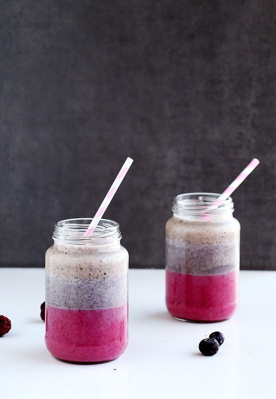 Layered smoothies in serving glasses with straws.