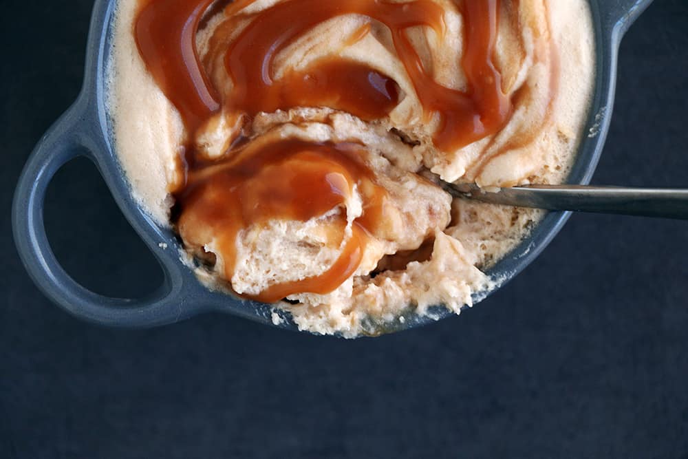 A serving of salted caramel mousse with a spoon and caramel sauce on a dark blue background.