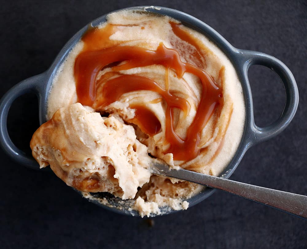A spoon digging into a caramel mousse with a drizzle of caramel sauce.