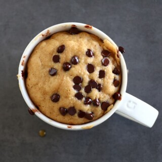 A peanut butter mug cake topped with mini chocolate chips served in a white mug.