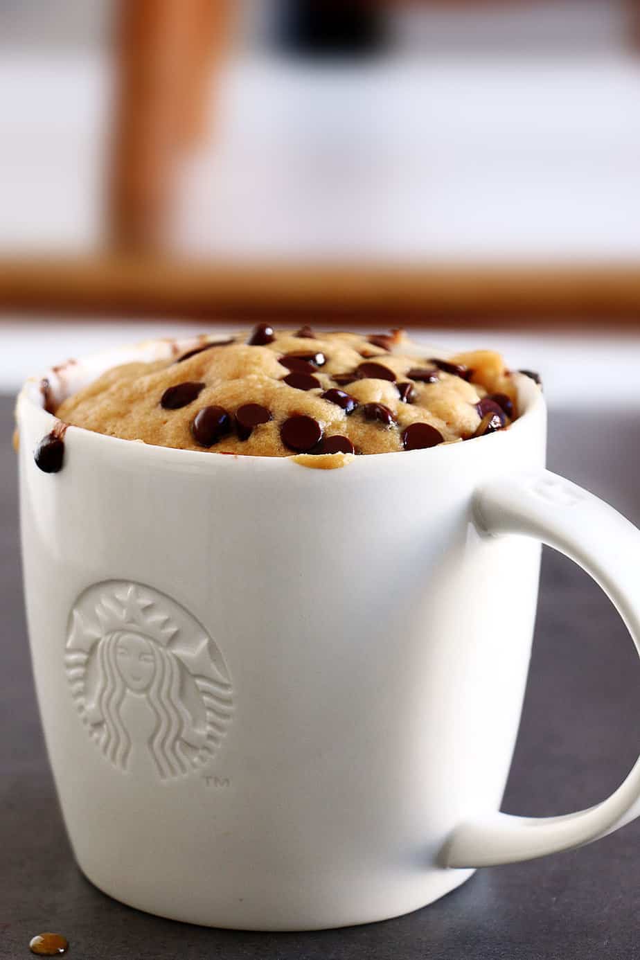 A cake in a white mug with chocolate chips.