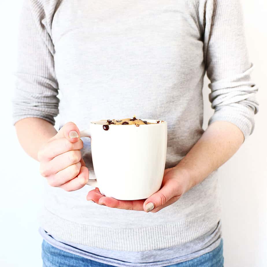 A person holding a  cake in a white mug.