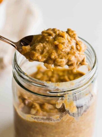 A spoon scooping up a bite of pumpkin pie overnight oats from a mason jar.