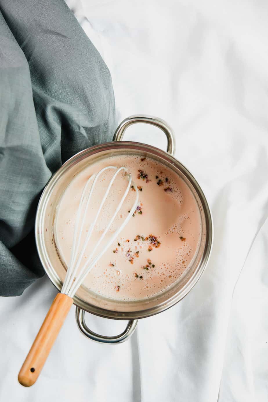 A pot with milky masala chai tea and spices and a white whisk.