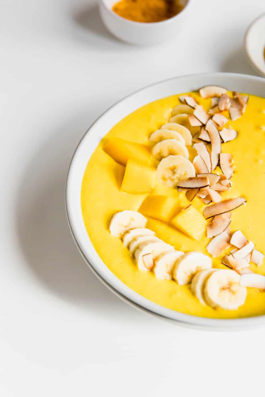 A smoothie bowl topped with chopped mango, banana, and coconut.