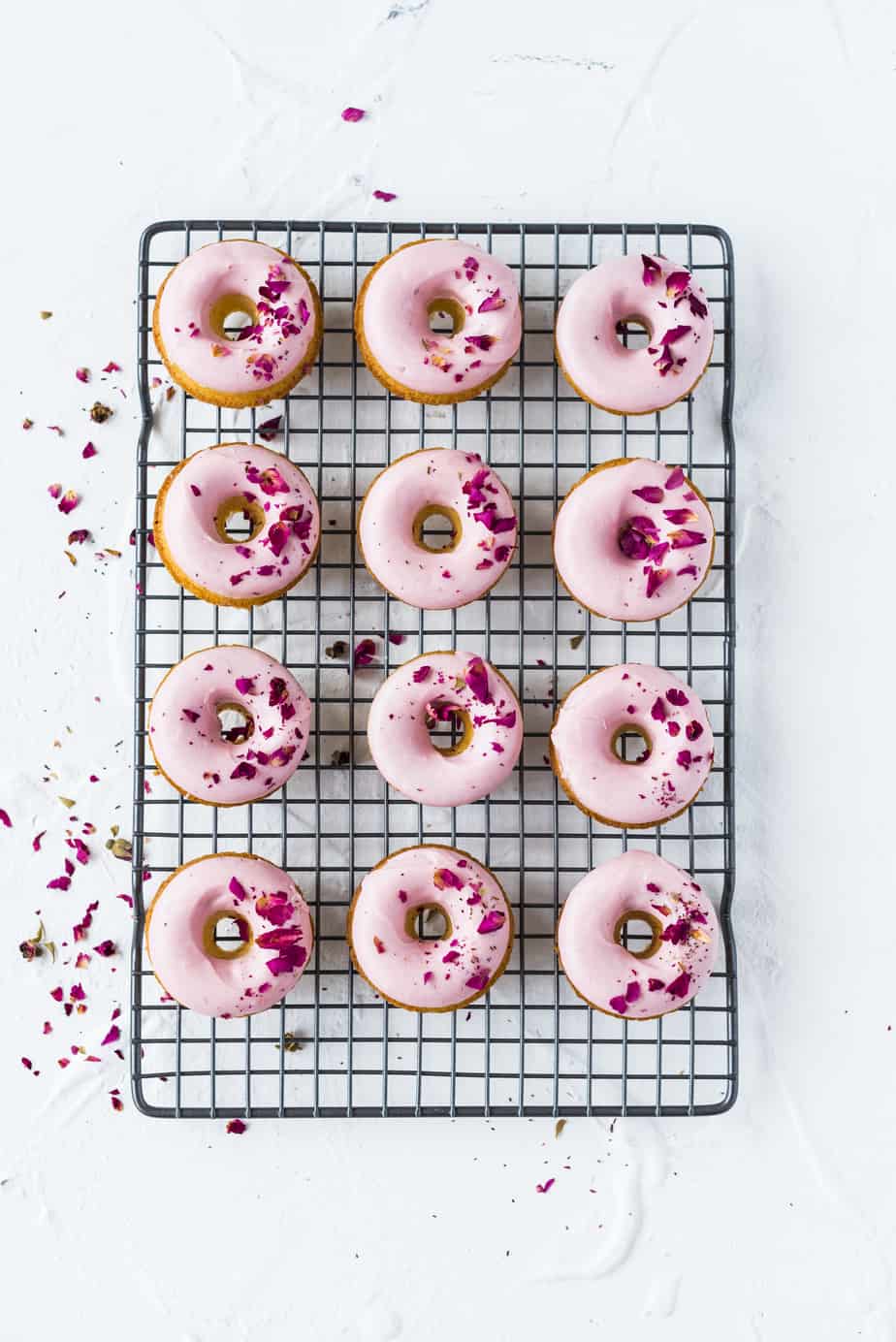 Glazed pink doughnuts on a cooling wrack.