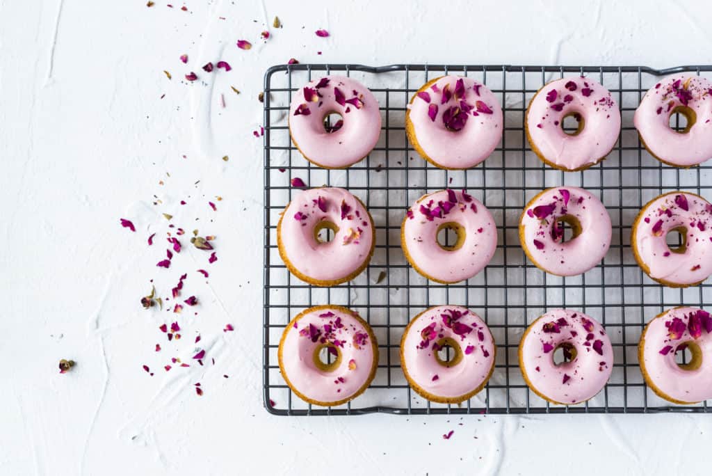 Pink glazed doughnuts on a black cooling wrack.