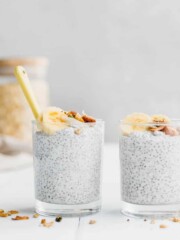 Two glasses of coconut cream chia pudding sitting on a white table.