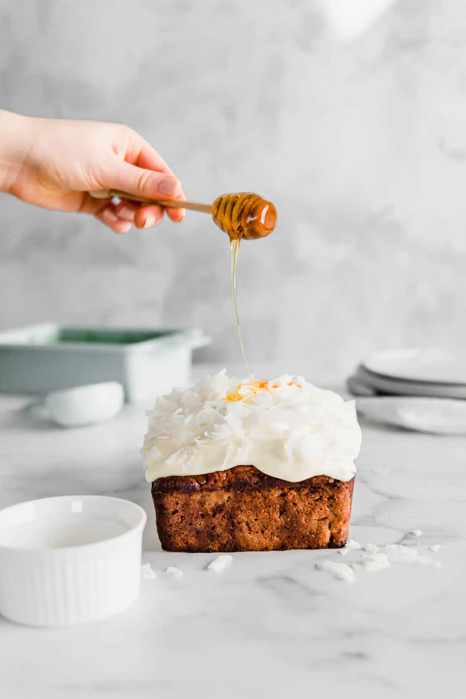 A person pouring honey over a frosted loaf.
