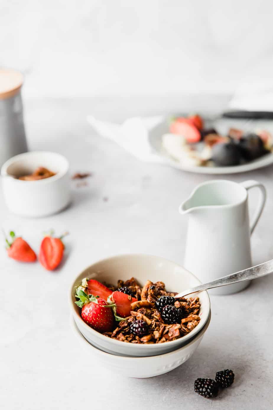 A white bowl filled with Crunchy Cinnamon Peanut Free Granola and fresh fruit with a silver spoon.