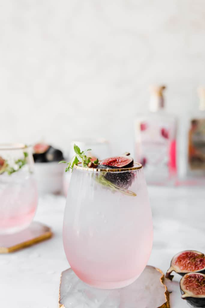 fig gin cocktail in pink glass with fresh figs and thyme leaves.