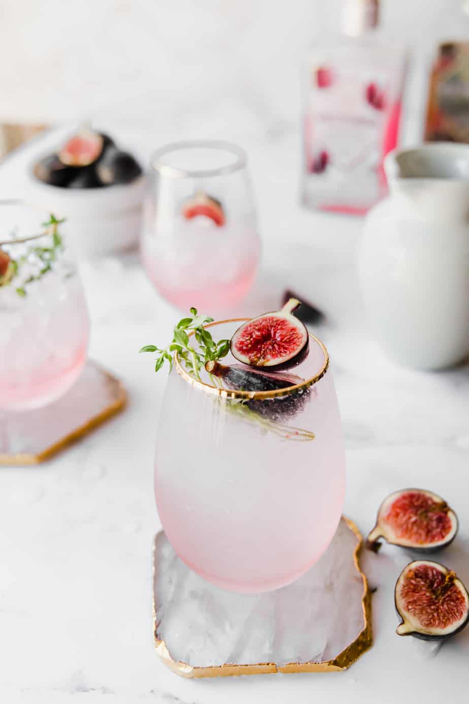 fig gin cocktail in pink glass with fresh figs and thyme leaves.