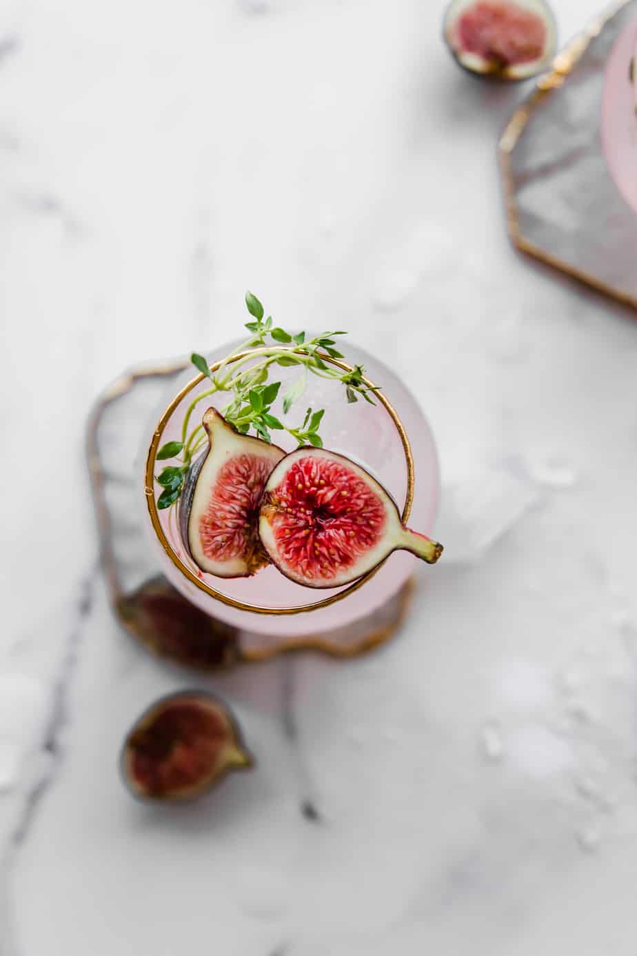 fig gin cocktail in pink glass with fresh figs and thyme leaves.