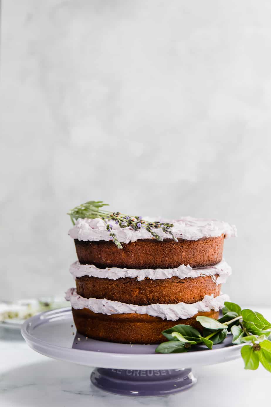 An Earl Grey Lavender Cake on a purple cake stand with fresh lavender.