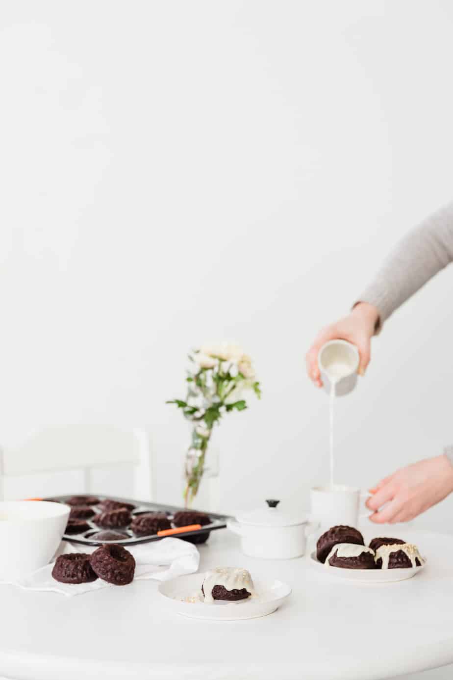 Mini bundt cakes on a white table with a person drinking coffee.