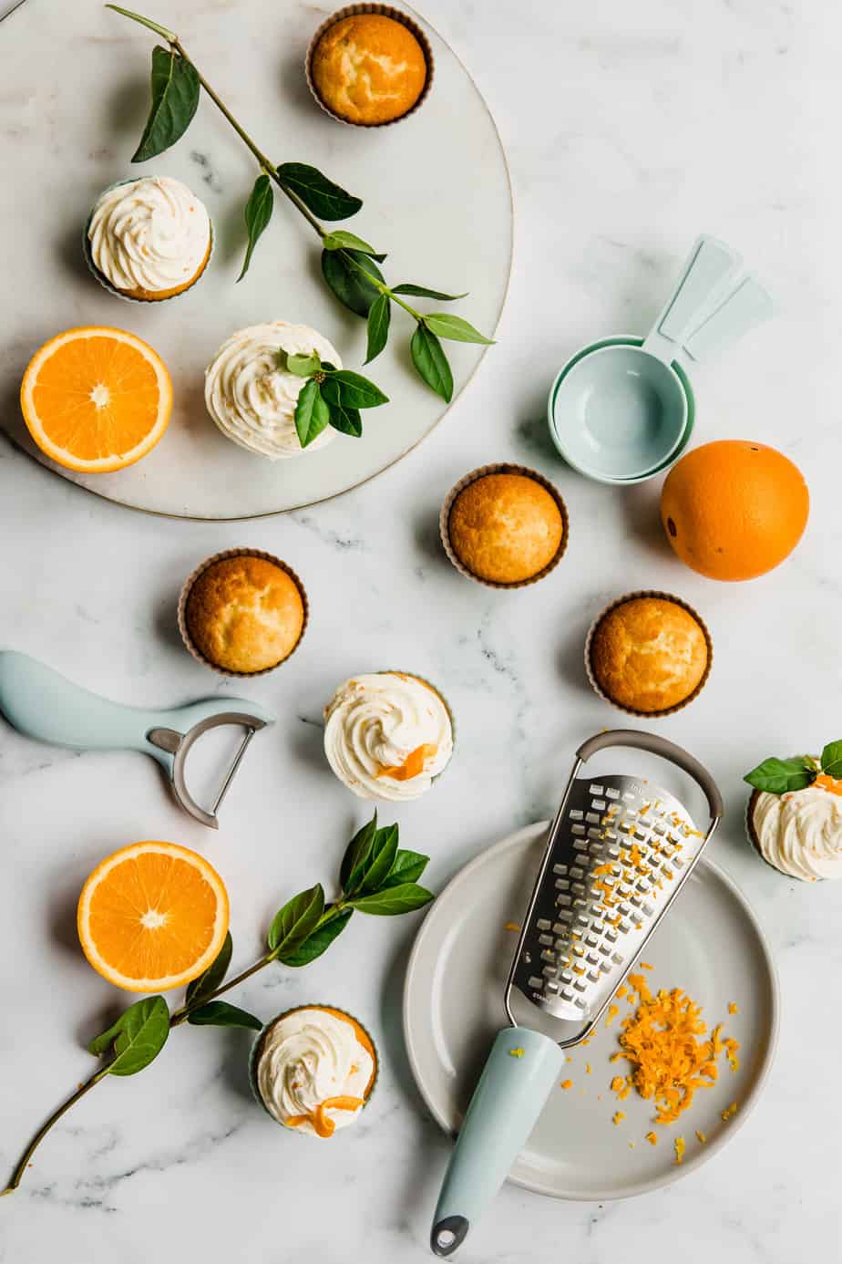 Vanilla cupcakes and fresh oranges on a marble background.