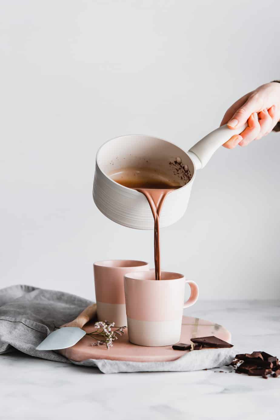 A small saucepan pouring hot chocolate into mugs.