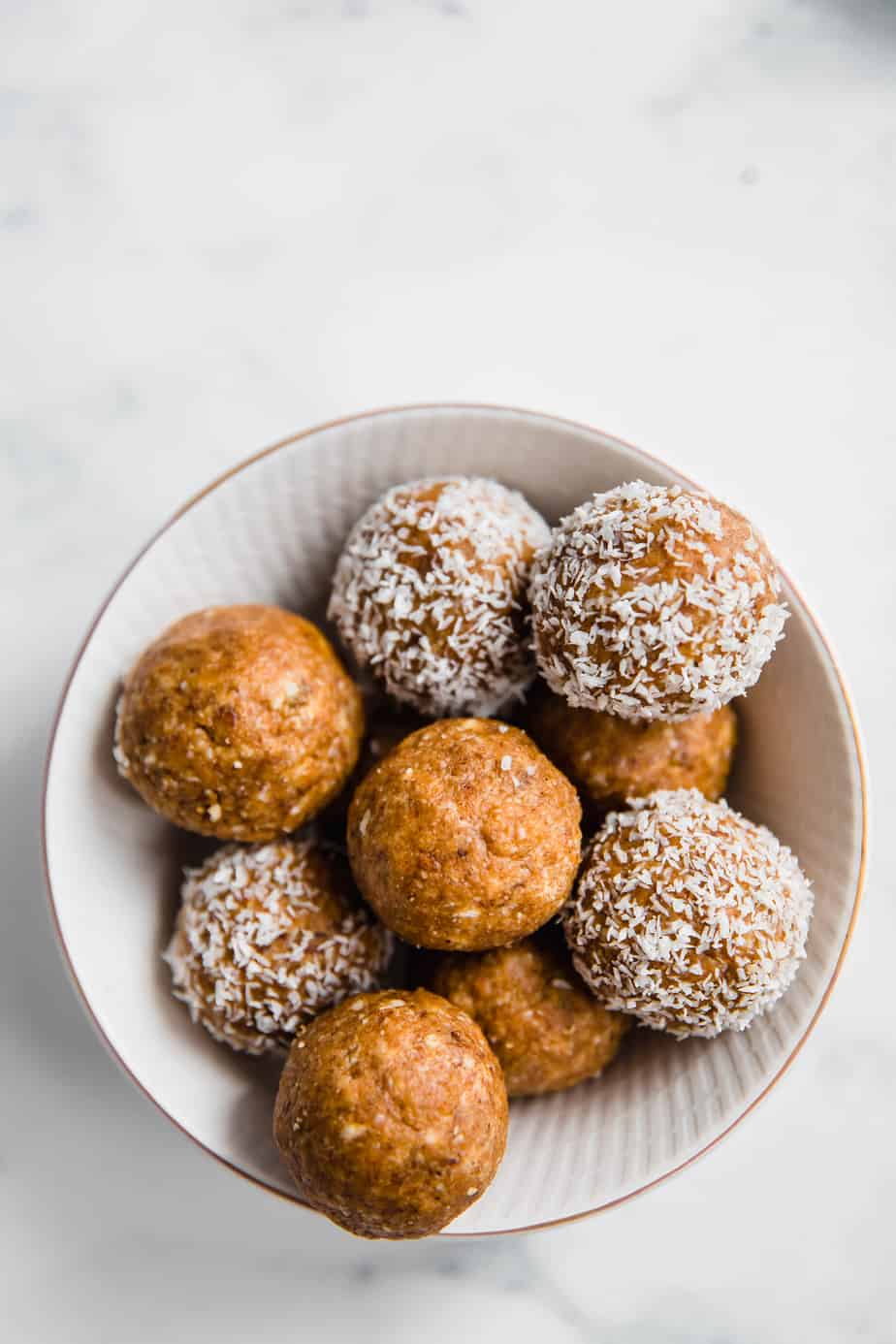 A bowl of no-bake date and coconut balls coated in coconut.