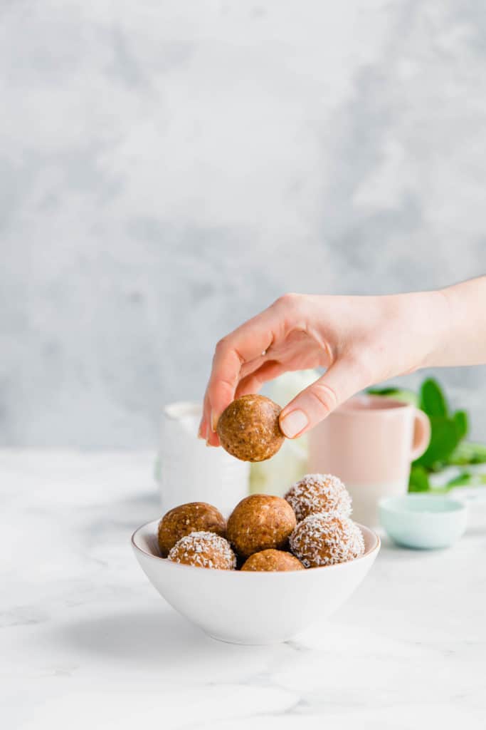 A bowl of energy balls with a hand reaching for one.