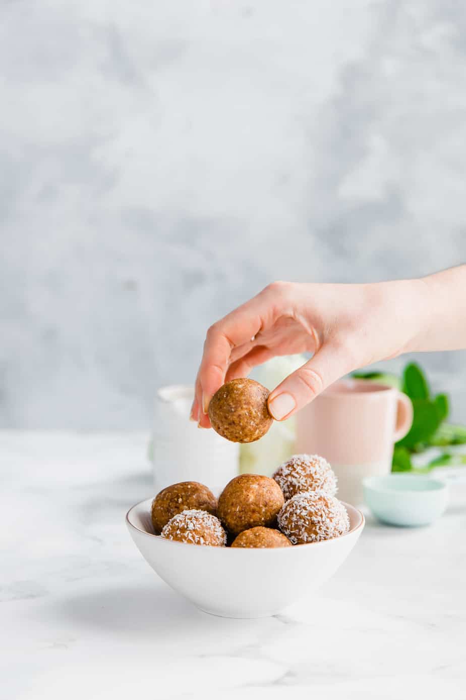 A bowl of energy balls with a hand reaching for one.