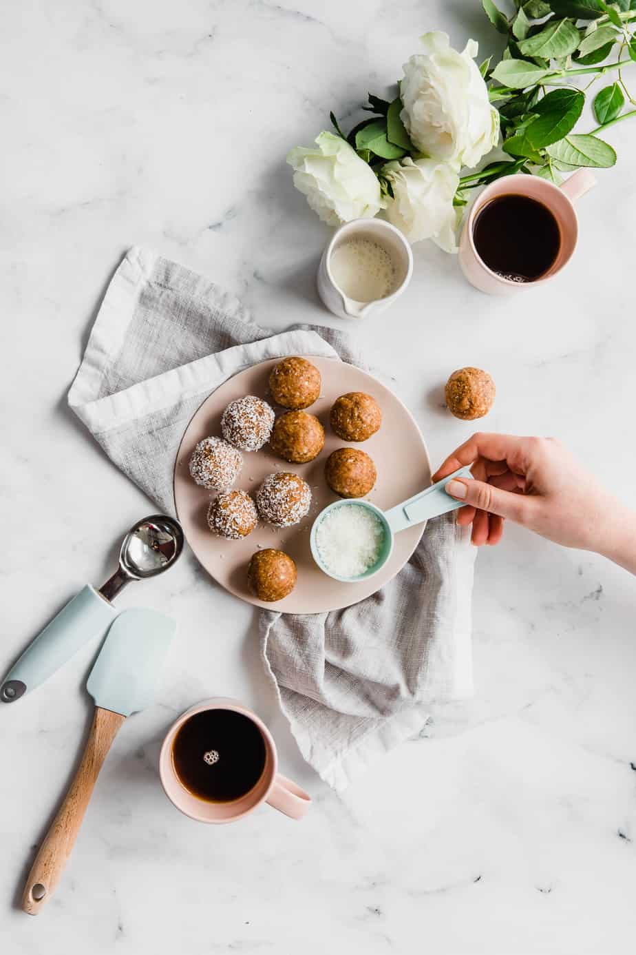 A plate of date and coconut balls with cups of coffee.