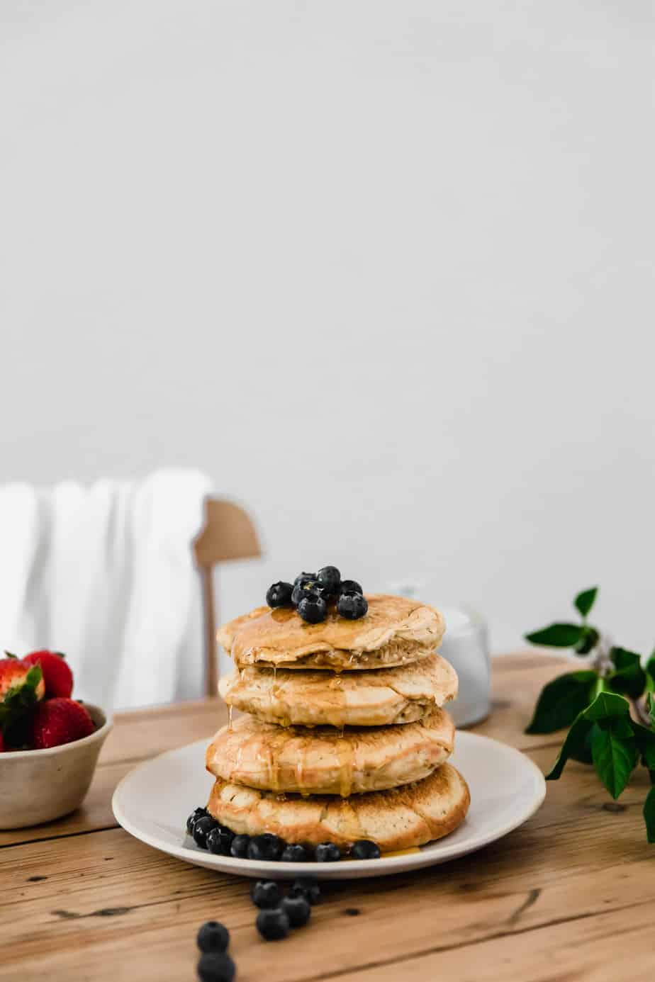 A stack of dairy-free pancakes with berries and honey on a wooden table.