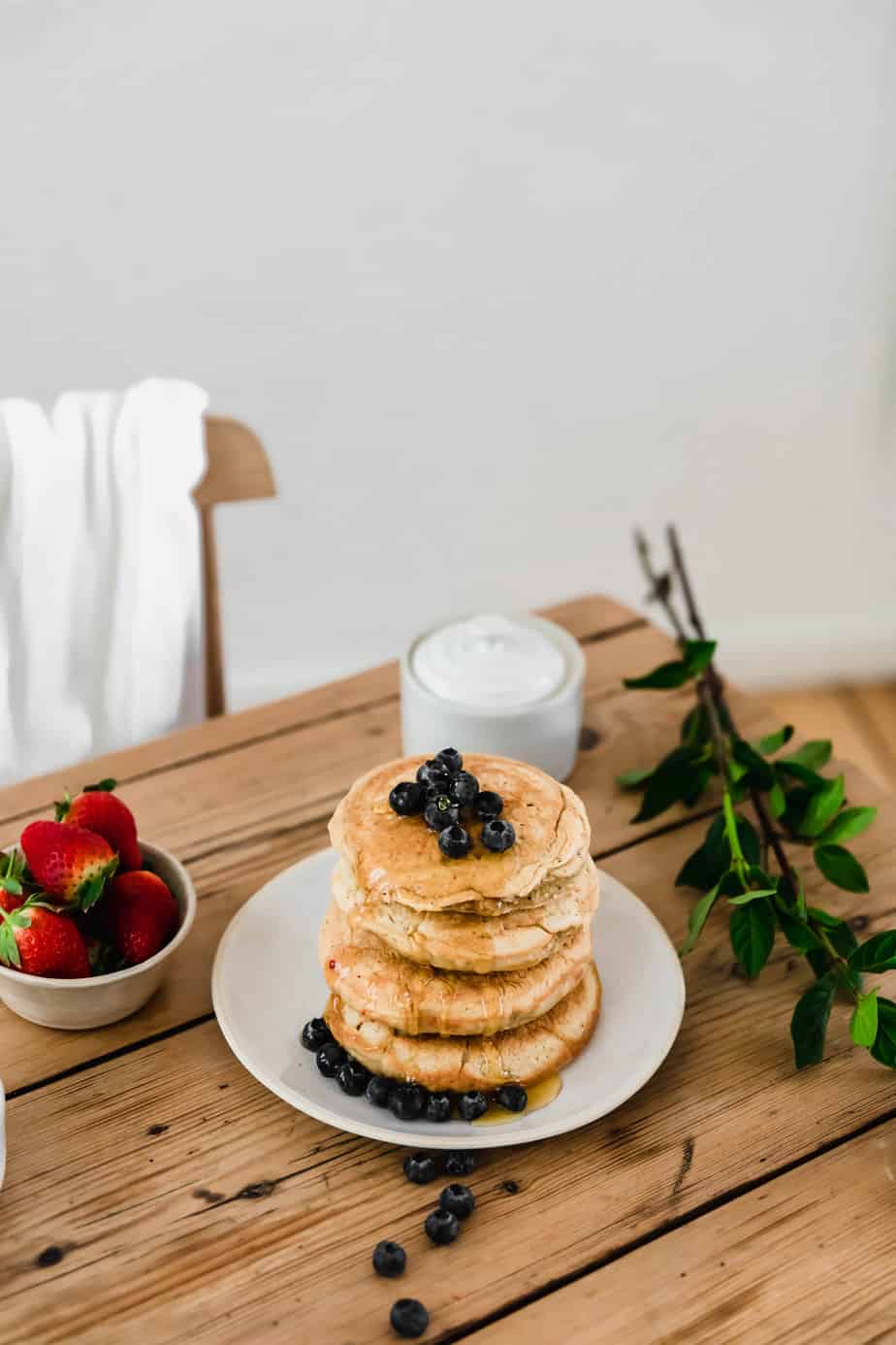 A stack of oat four pancakes on a white plate with berries.