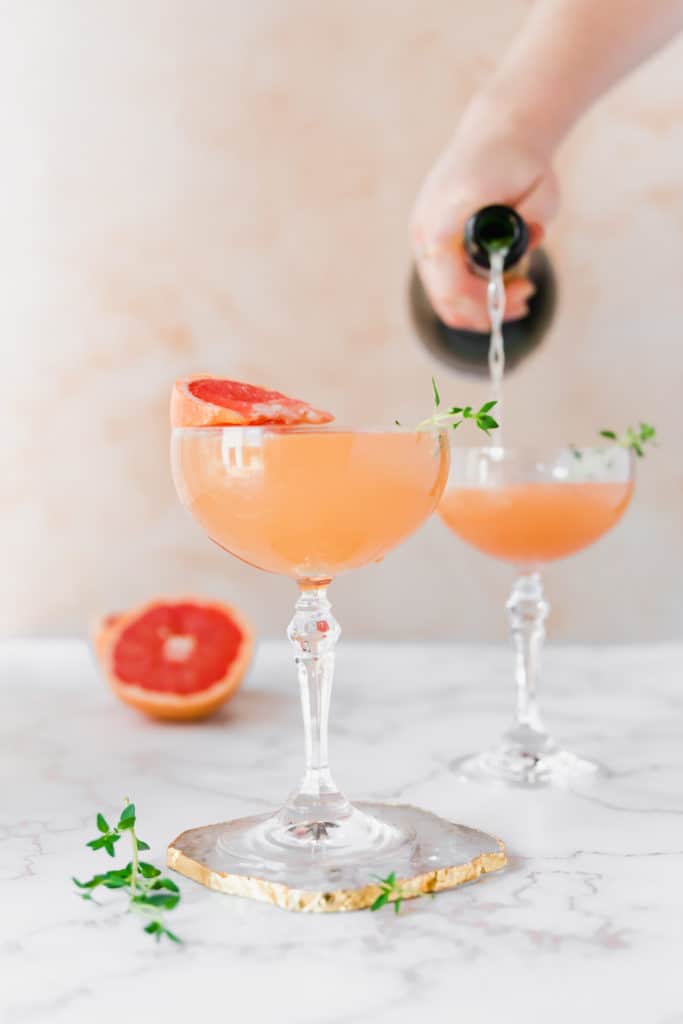 Two cocktail glasses garnished with fresh thyme sprigs.
