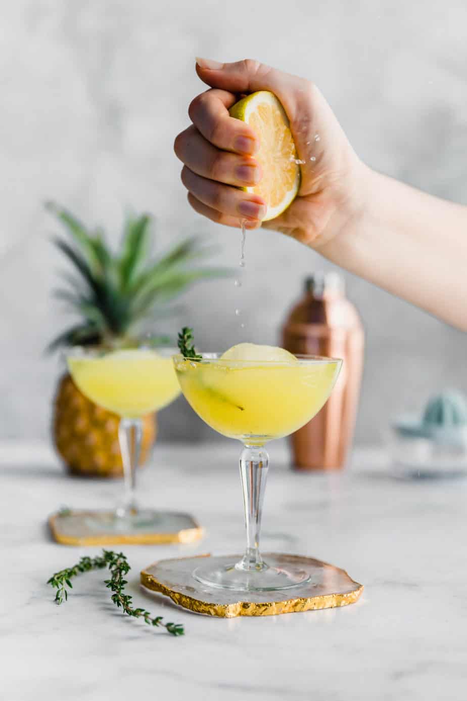 A hand squeezing fresh lemon into a pineapple gin & ginger beer cocktail.