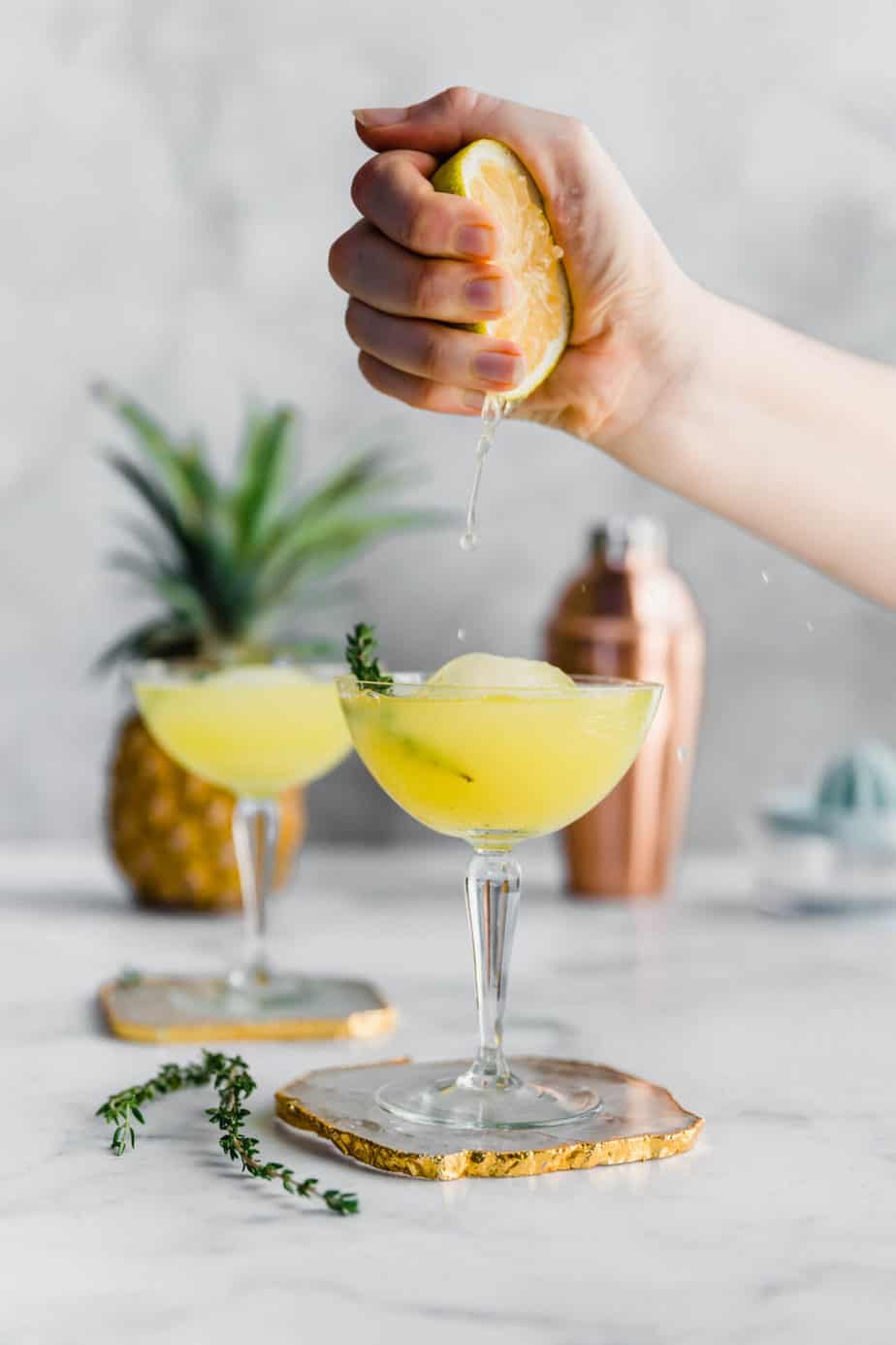A hand squeezing a lemon into a vodka drink with pineapple.