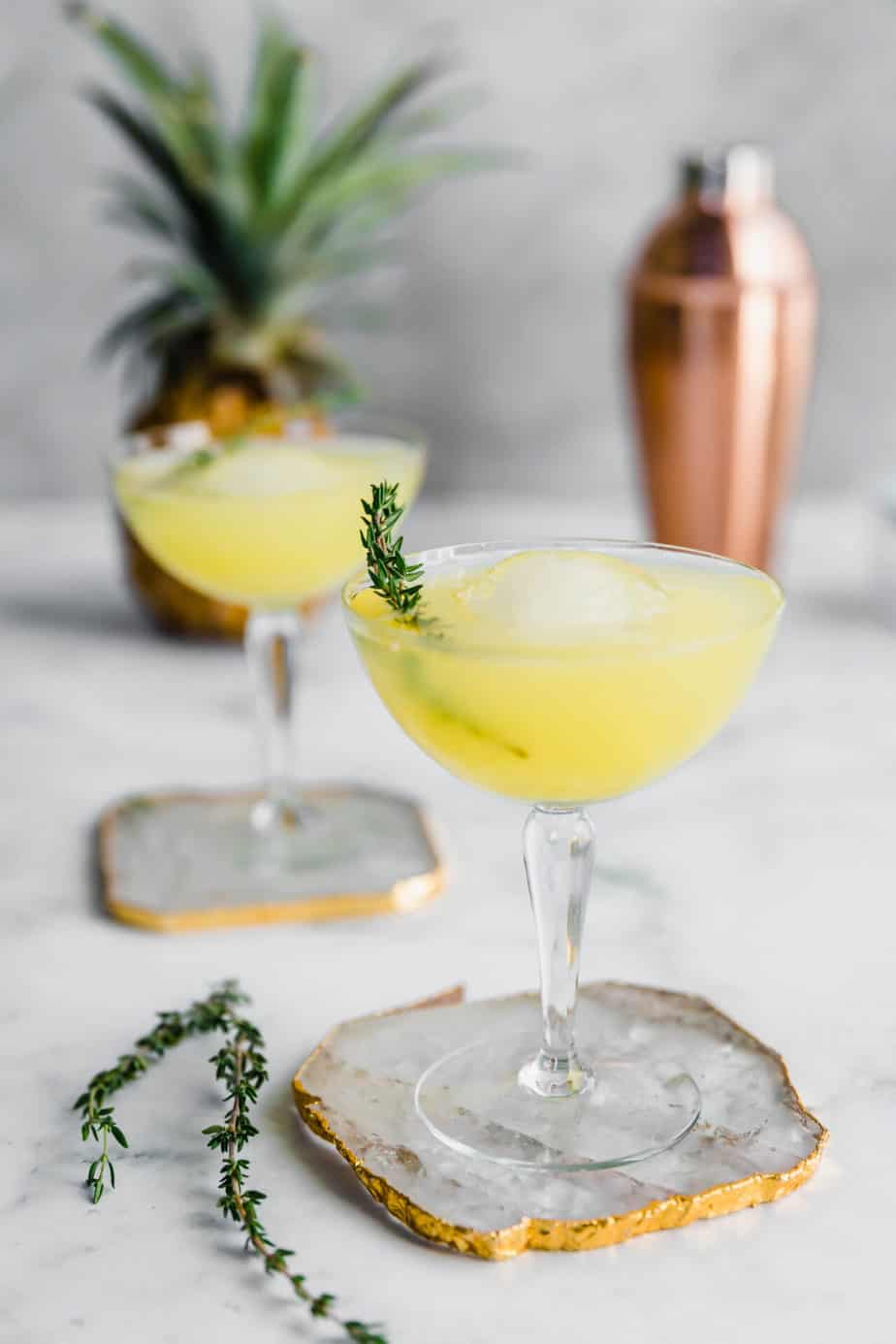 Two Pineapple & Ginger Cocktails served with ice and a sprig of fresh thyme.