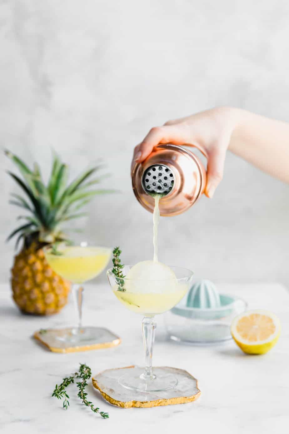 A pineapple vodka cocktail being poured into a serving glass from a cocktail shaker.