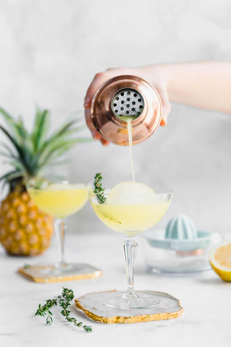 A cocktail shaker filling a serving glass with pineapple gin cocktail.