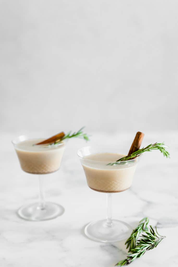 Two creamy cocktails in martini glasses with fresh rosemary.