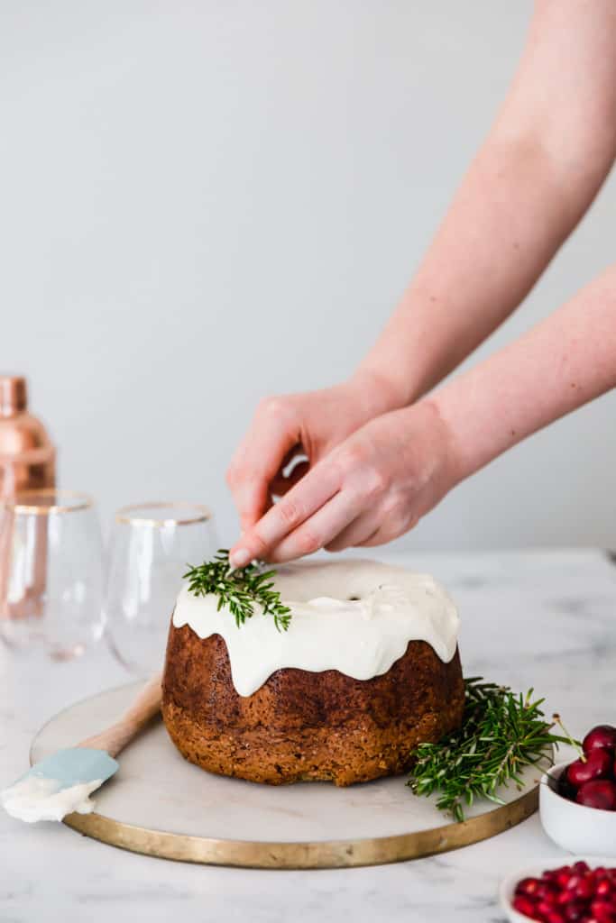 Fresh rosemary being placed on top of a gingerbread bundt cake.