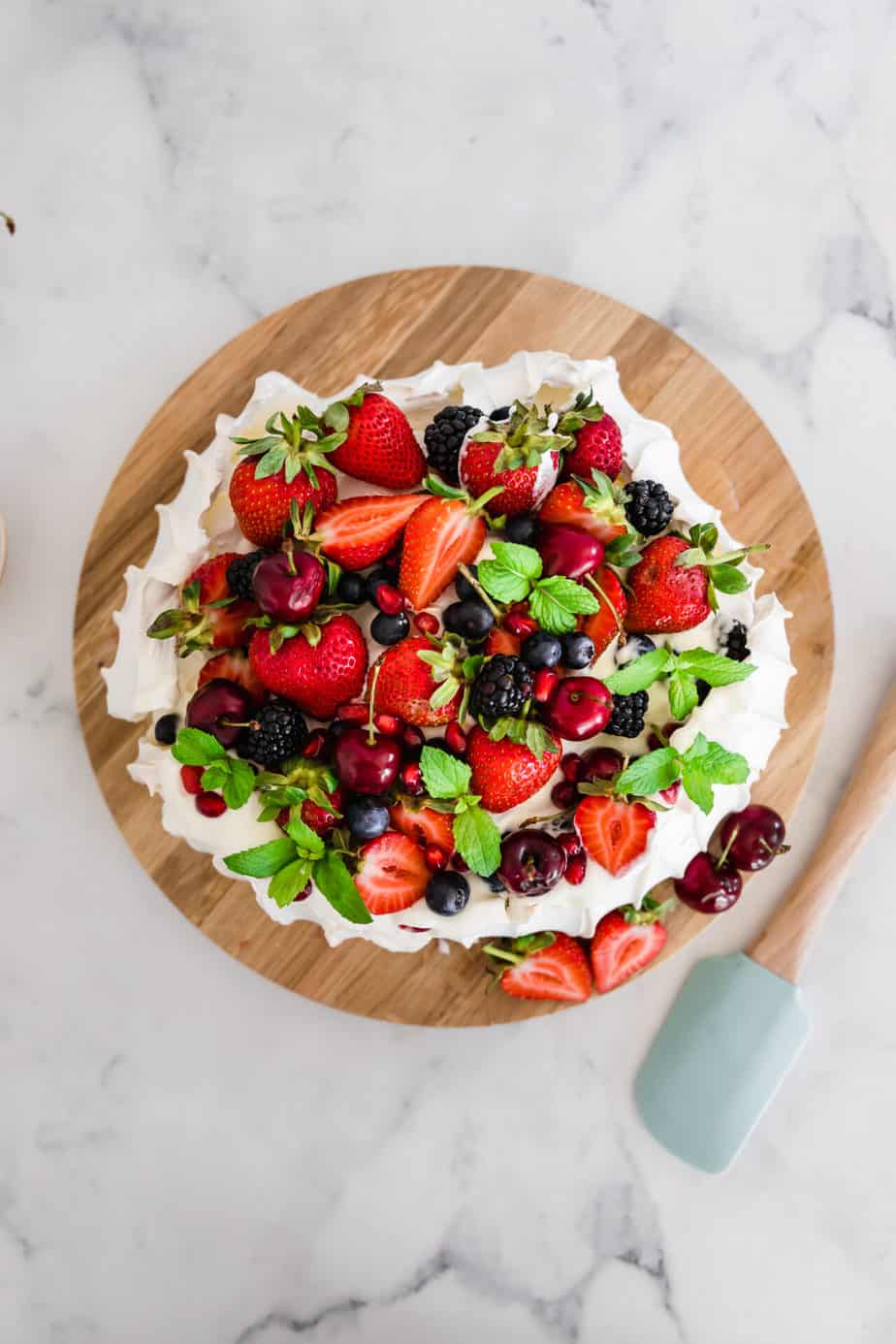 A pavlova topped with mixed berries and fresh mint